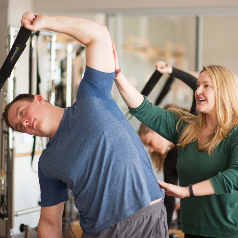 Woman helping man stretch his arm at TWC Pilates