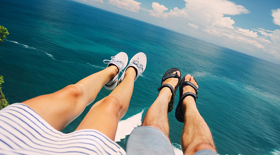 woman and man hanging legs over ledge by ocean