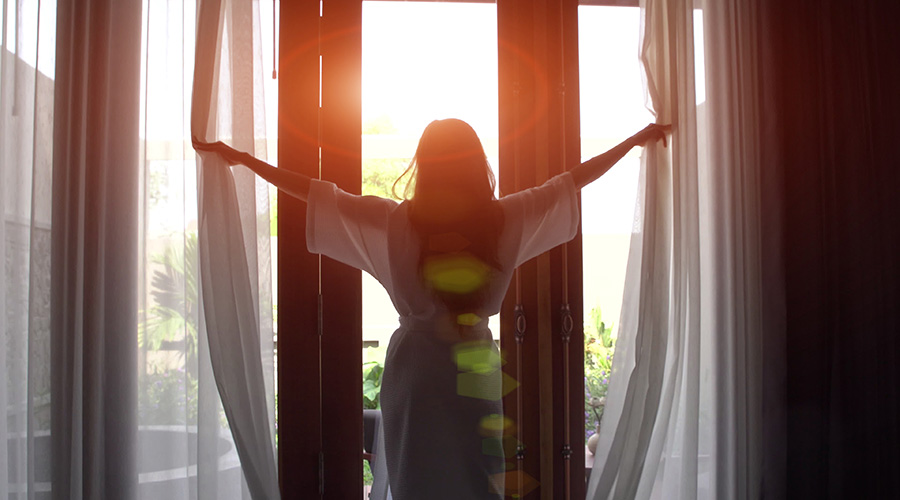 woman opening curtains during a sunrise