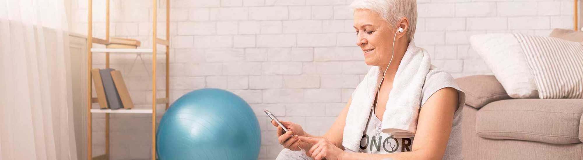 senior woman working out with phone at home with honor yoga