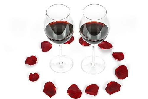 two glasses of red wine surrounded by rose petals