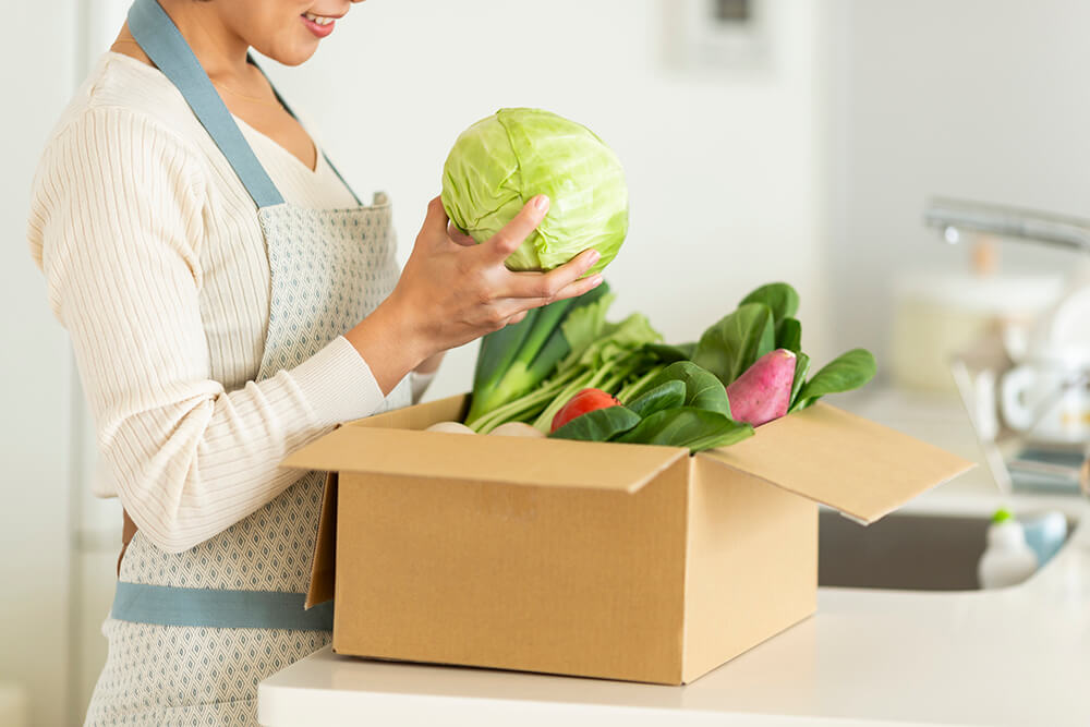 woman opening a box of vegetables in leora's kitchen