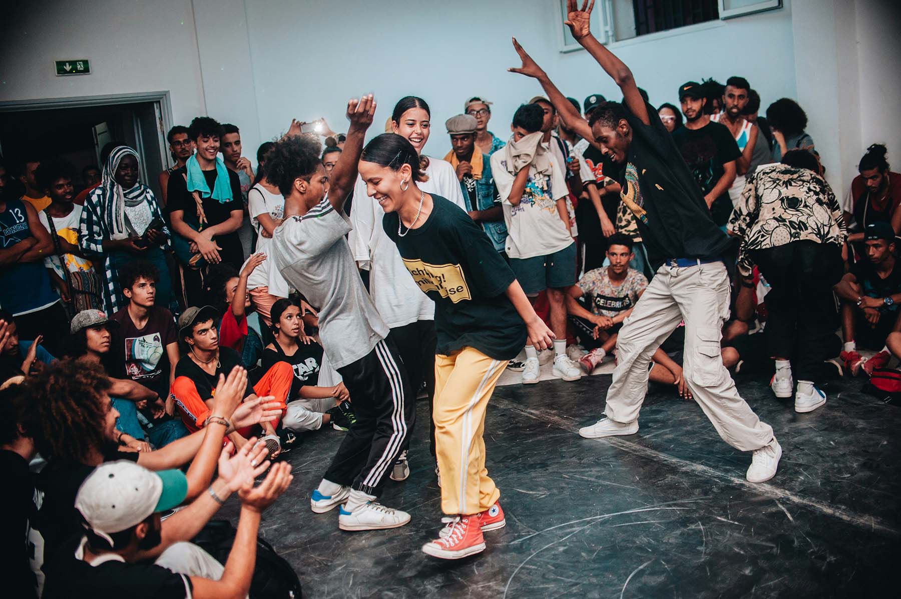 A lively group of dancers performing in a circle with an enthusiastic crowd cheering them on, creating an inspiring atmosphere of dance and community spirit