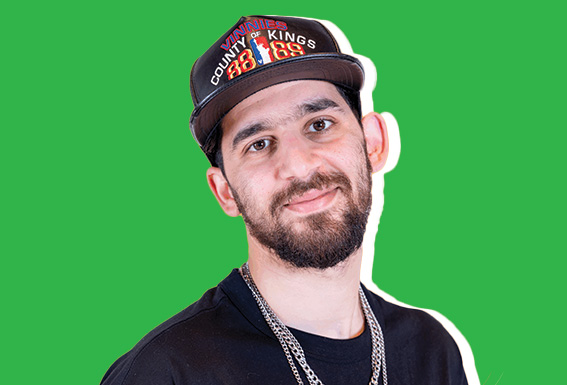 Waldo smiles casually in front of a green background, wearing a black shirt, layered chains, and a baseball cap that reads “County of Kings.”