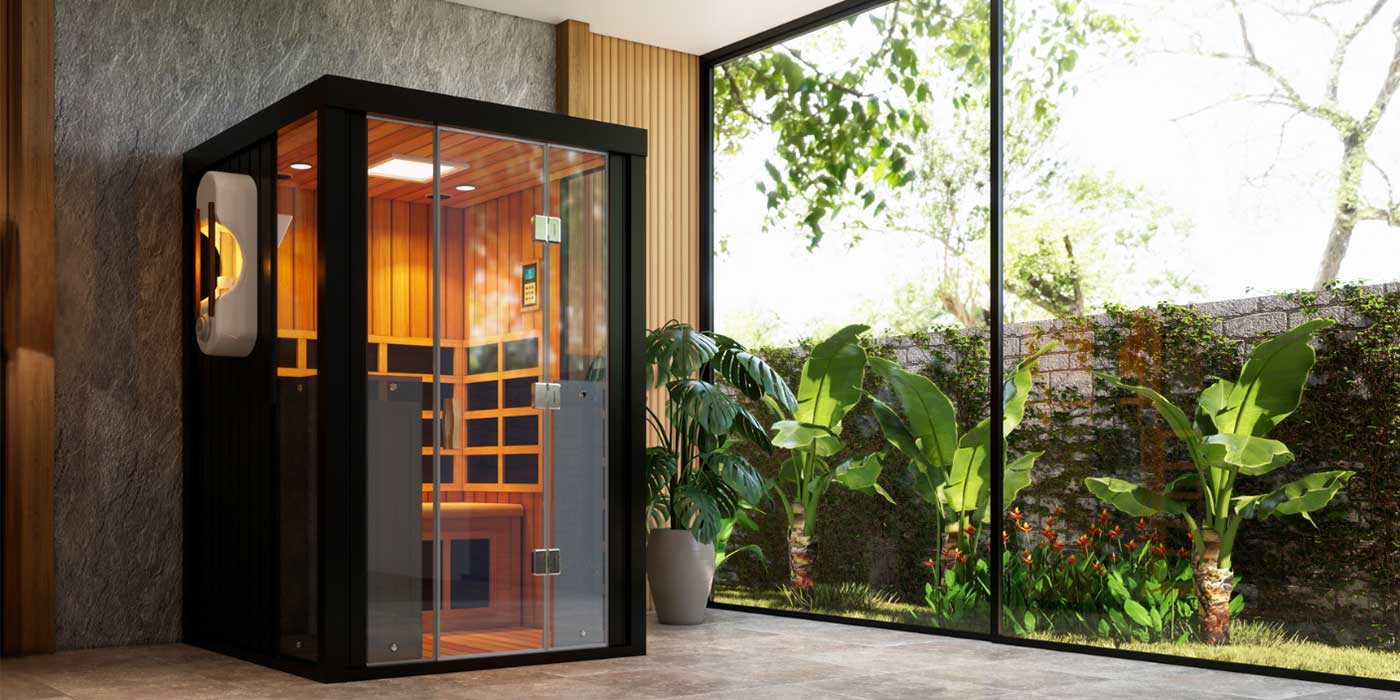 A black-framed indoor sauna against a wooden and stone wall wooden interior with a glass window looking onto flowers and a stone wall.