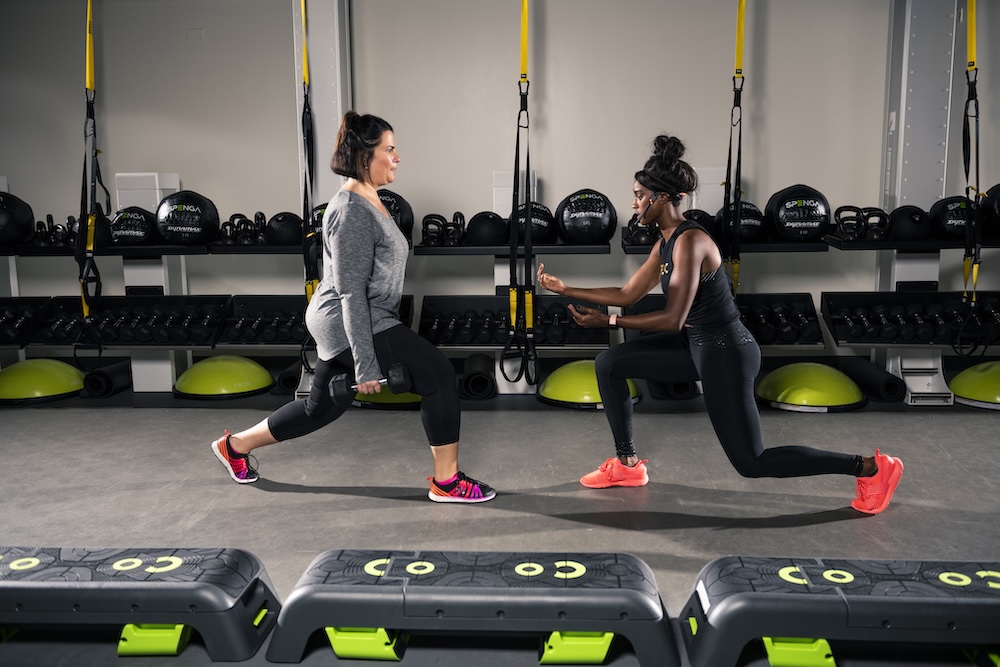 Two people at SPENGA Malbrough stretching in front of a wall of weights. 