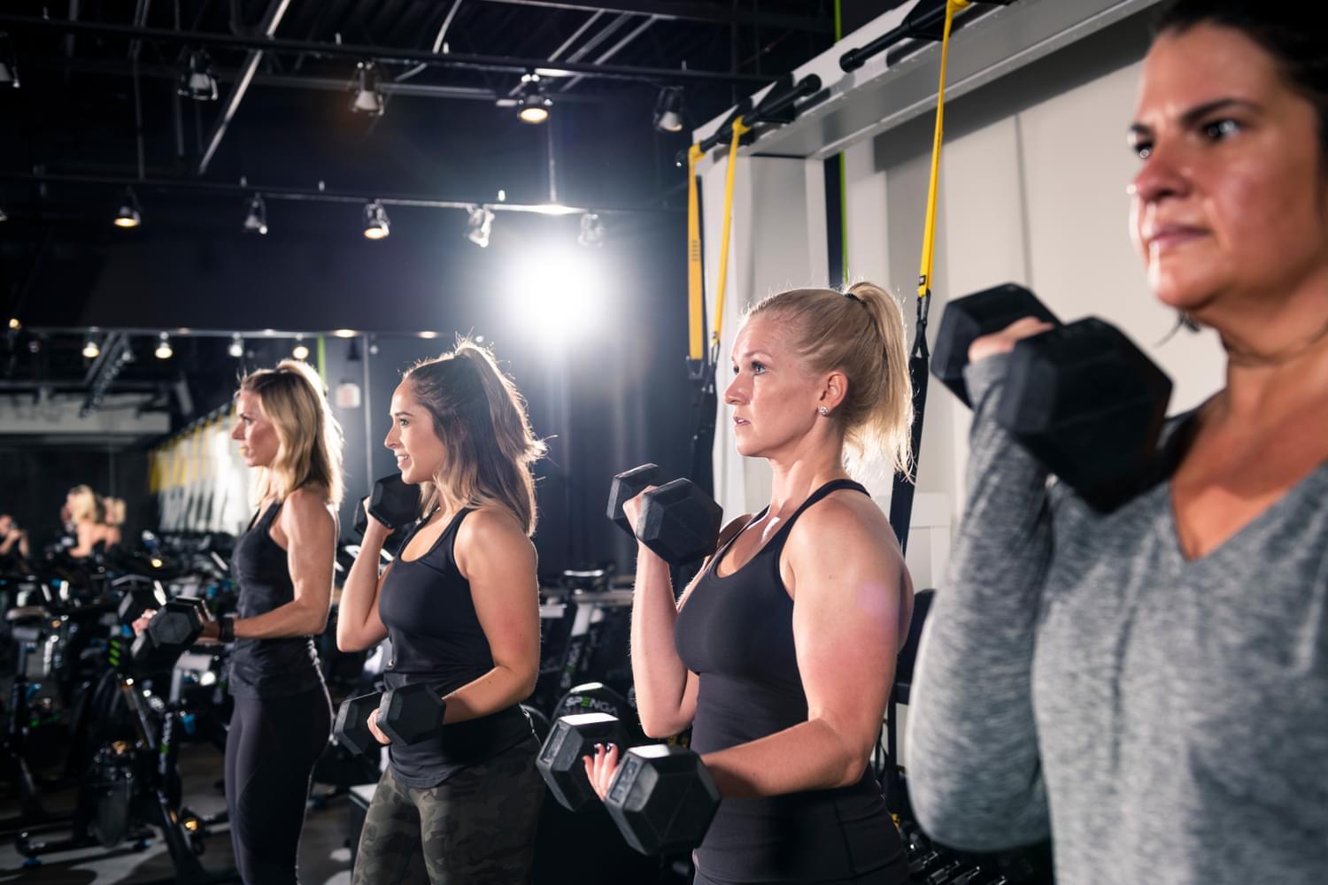  A group of adults, including seniors, performing strength training exercises with dumbbells in a gym setting, showcasing an active and healthy lifestyle.