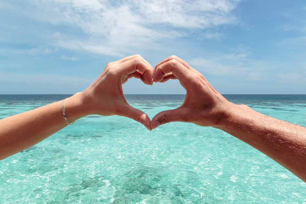 hands forming a heart at the ocean