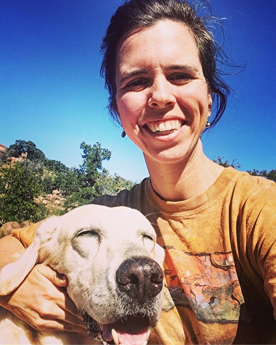 a smiling woman with her dog during a hike on a sunny day